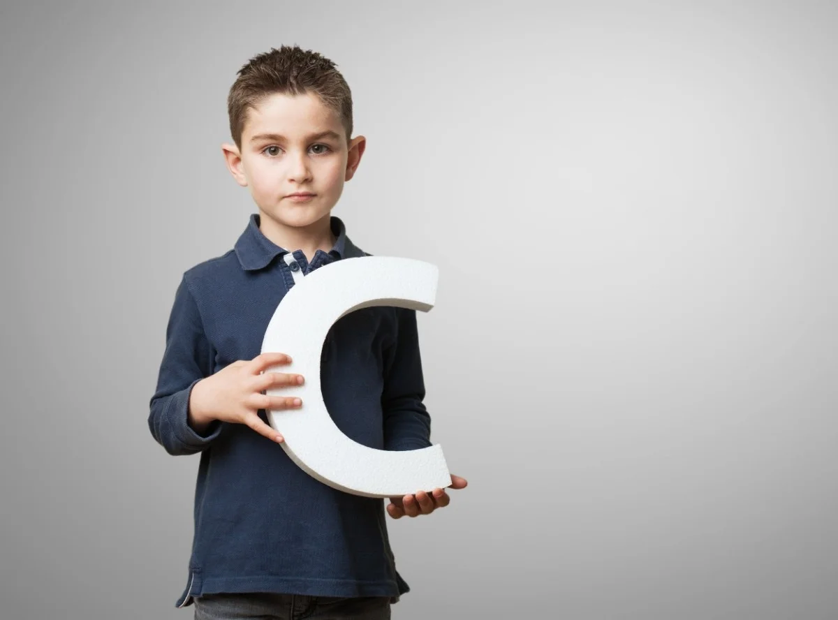A young child holding a large white letter "C" against a neutral background, symbolizing the beginning of various acronyms. Acronyms Starting with C: Common, Technical & Business Terms